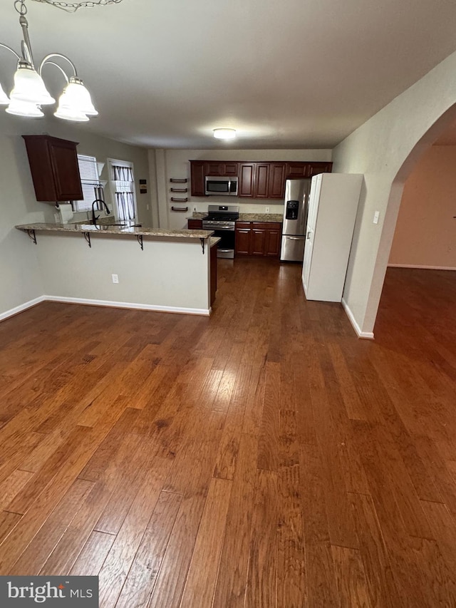 kitchen with a breakfast bar, dark hardwood / wood-style flooring, kitchen peninsula, stainless steel appliances, and a chandelier