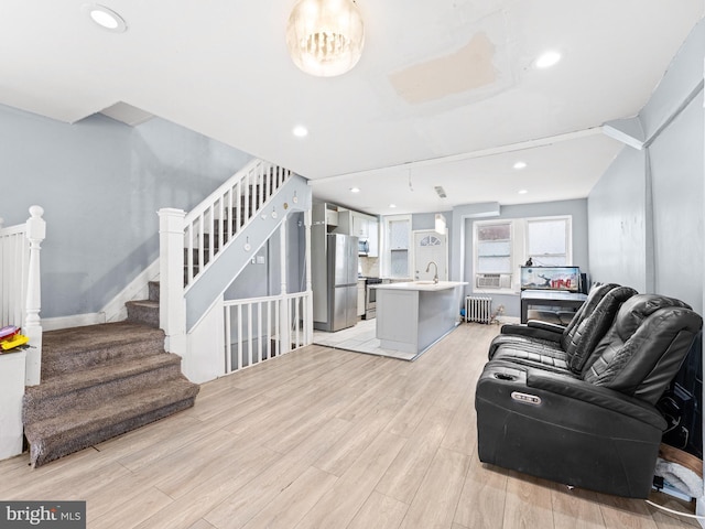 living room with lofted ceiling, radiator heating unit, sink, and light hardwood / wood-style flooring