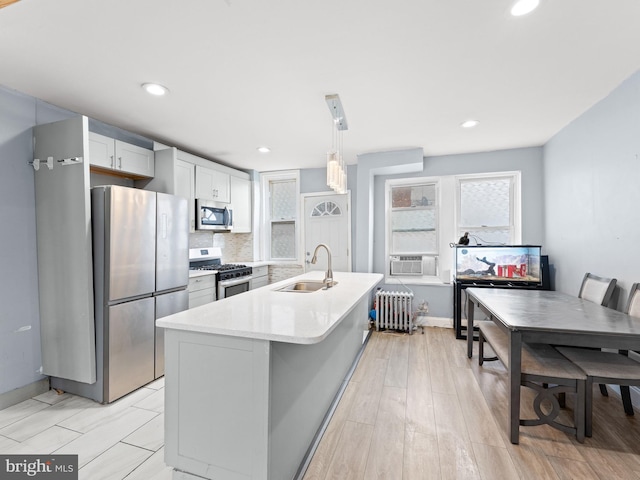 kitchen with sink, appliances with stainless steel finishes, radiator heating unit, tasteful backsplash, and decorative light fixtures