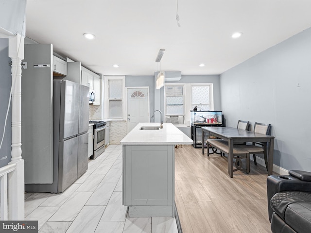 kitchen with pendant lighting, sink, gray cabinetry, stainless steel appliances, and a center island with sink