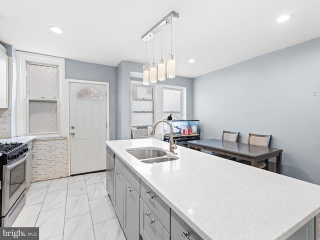 kitchen with sink, light stone counters, decorative light fixtures, a center island with sink, and stainless steel appliances