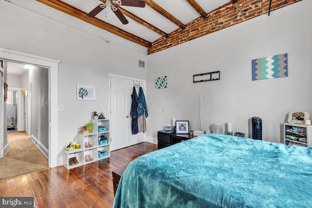 bedroom with beam ceiling, a closet, visible vents, a towering ceiling, and hardwood / wood-style flooring