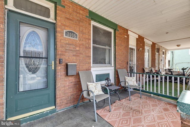 doorway to property with a porch and brick siding