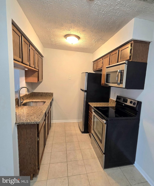 kitchen with a textured ceiling, dark stone counters, appliances with stainless steel finishes, light tile patterned flooring, and sink