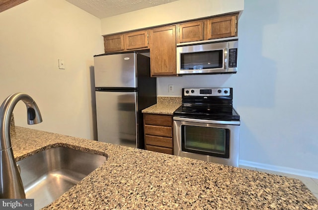 kitchen featuring appliances with stainless steel finishes, light stone counters, a textured ceiling, and sink