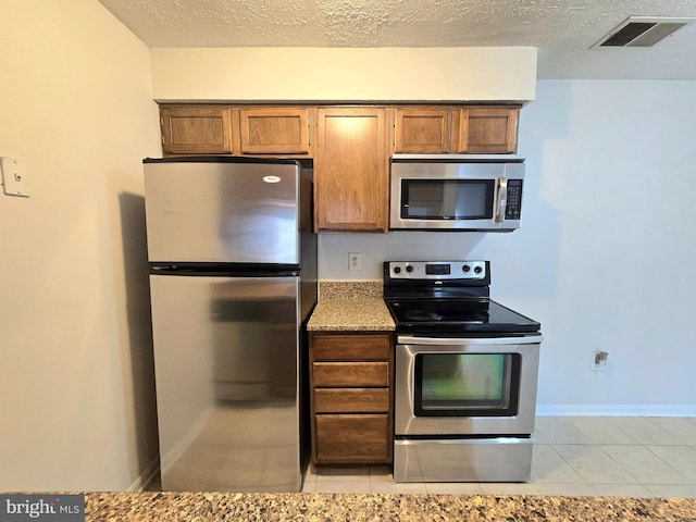 kitchen with stainless steel appliances, a textured ceiling, stone countertops, and light tile patterned floors