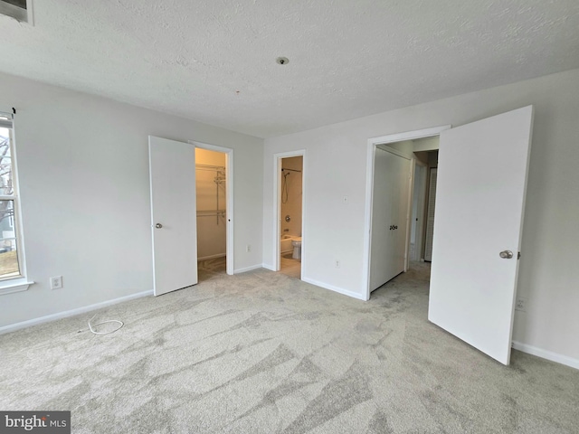 unfurnished bedroom with a textured ceiling, a spacious closet, ensuite bathroom, a closet, and light colored carpet