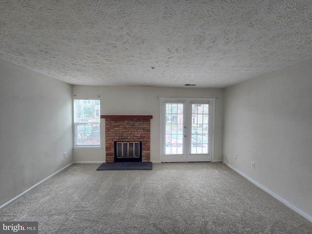 unfurnished living room featuring french doors, a brick fireplace, a textured ceiling, and carpet