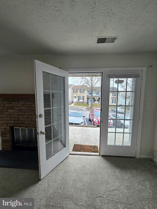 doorway featuring french doors, a textured ceiling, a fireplace, and carpet floors