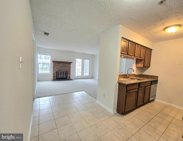 kitchen featuring light carpet, a fireplace, a textured ceiling, stainless steel dishwasher, and sink