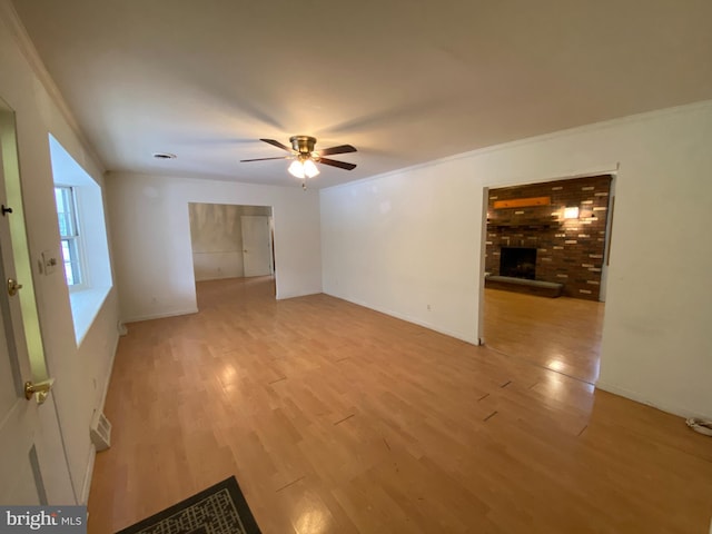 unfurnished room featuring a brick fireplace, ceiling fan, light hardwood / wood-style floors, and ornamental molding