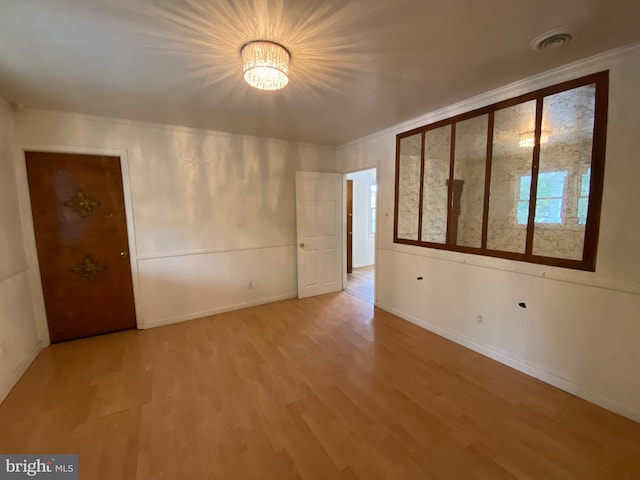 unfurnished room with ornamental molding, light wood-type flooring, and an inviting chandelier