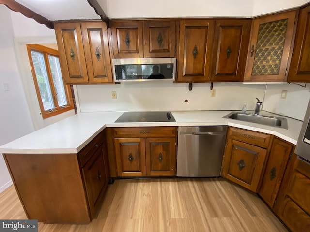 kitchen with sink, kitchen peninsula, light hardwood / wood-style flooring, and appliances with stainless steel finishes