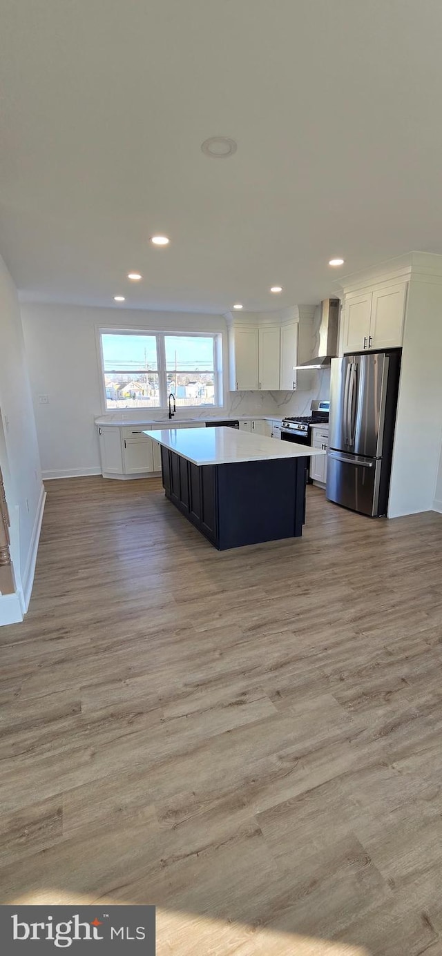 kitchen featuring wall chimney exhaust hood, stainless steel appliances, a center island, light hardwood / wood-style floors, and white cabinetry