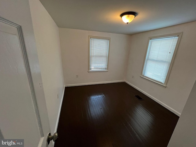 empty room with dark hardwood / wood-style floors and plenty of natural light