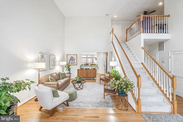 living room with a high ceiling, ceiling fan with notable chandelier, and light hardwood / wood-style flooring