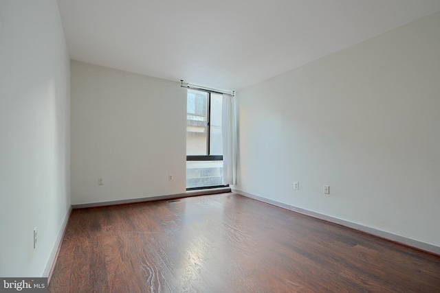 empty room with a wall of windows and dark hardwood / wood-style floors