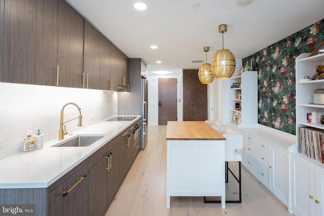 kitchen featuring pendant lighting, sink, white cabinets, light hardwood / wood-style floors, and dark brown cabinets