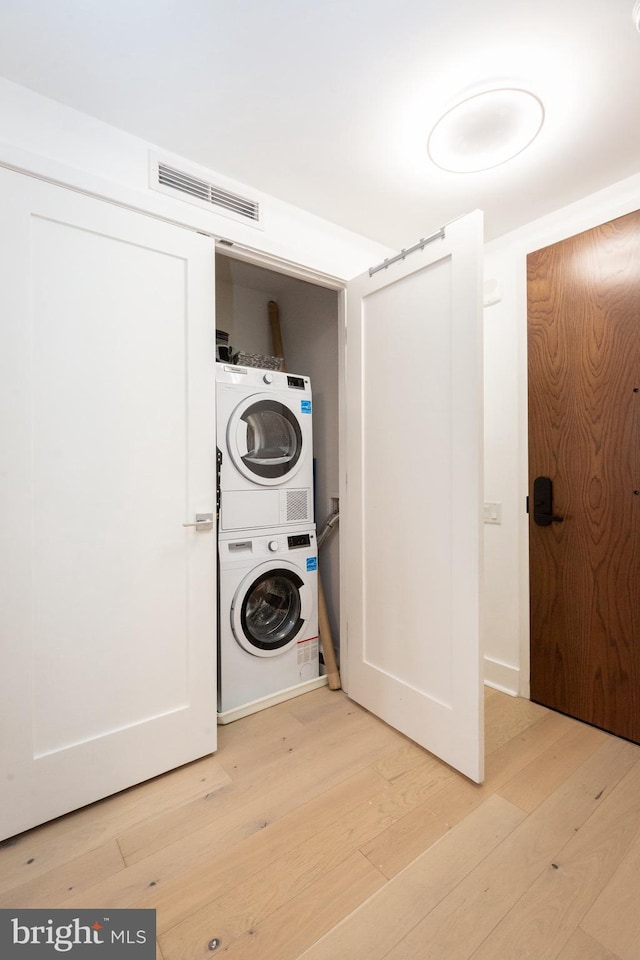 laundry room featuring stacked washer and dryer and light hardwood / wood-style flooring