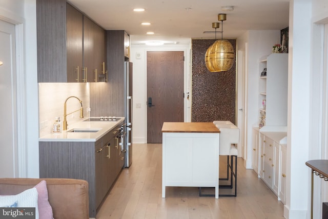 kitchen with sink, stainless steel fridge, a kitchen breakfast bar, hanging light fixtures, and light hardwood / wood-style floors