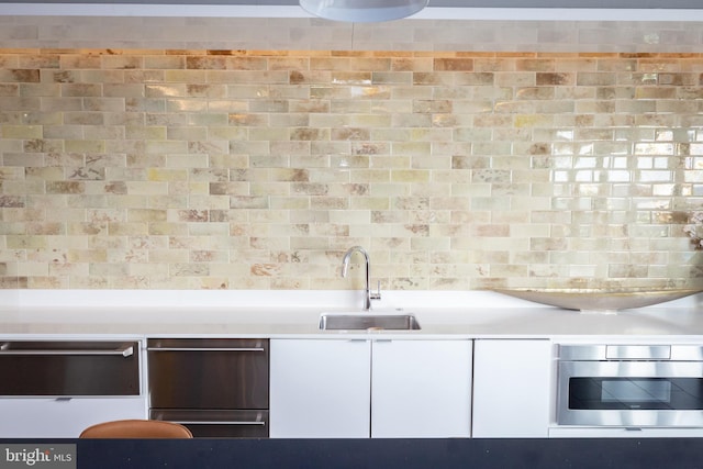 kitchen with white cabinetry, sink, oven, and backsplash