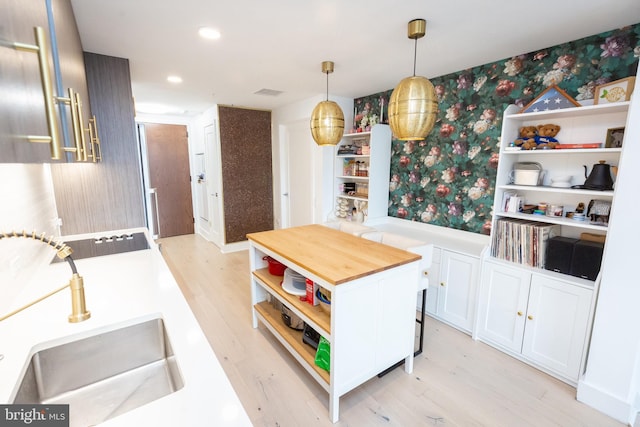 kitchen featuring decorative light fixtures, white cabinetry, sink, black electric cooktop, and light hardwood / wood-style flooring