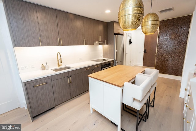 kitchen with dark brown cabinetry, sink, stainless steel refrigerator, black electric cooktop, and wall oven