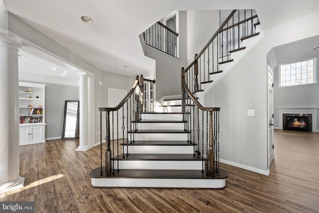 stairway with wood-type flooring, built in features, crown molding, and ornate columns