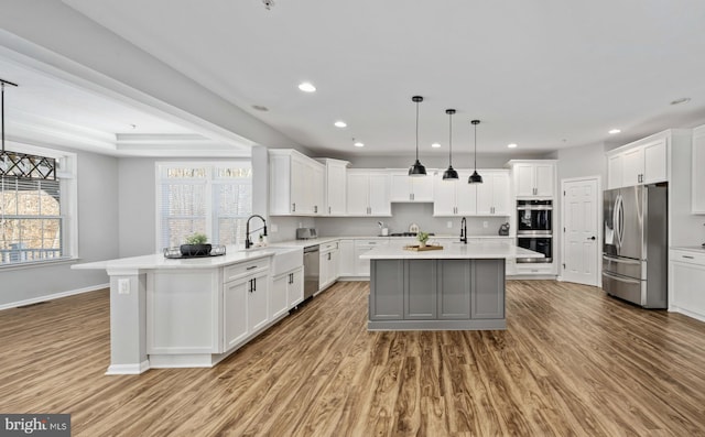 kitchen featuring hardwood / wood-style floors, a center island with sink, appliances with stainless steel finishes, hanging light fixtures, and white cabinets