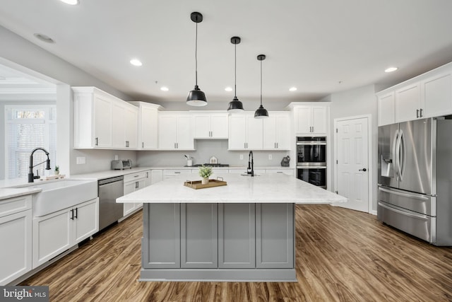 kitchen with white cabinets, appliances with stainless steel finishes, sink, a kitchen island with sink, and light stone counters