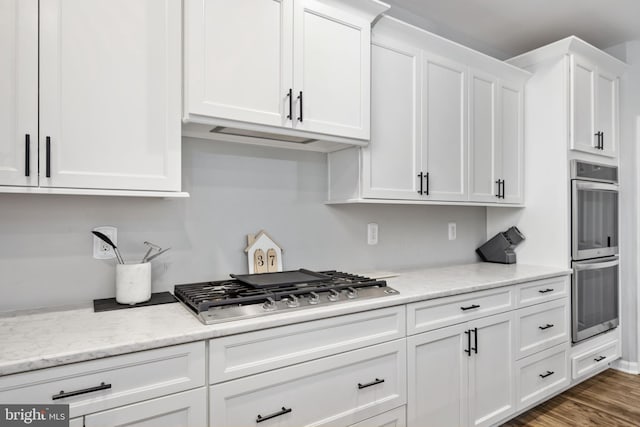 kitchen featuring dark hardwood / wood-style floors, appliances with stainless steel finishes, white cabinets, and light stone counters