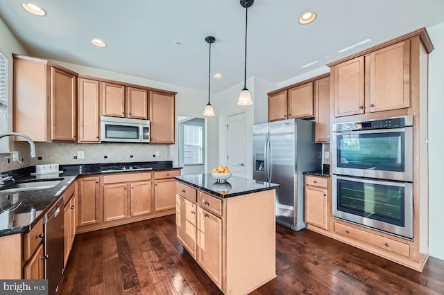 kitchen featuring decorative light fixtures, dark stone countertops, a center island, sink, and stainless steel appliances