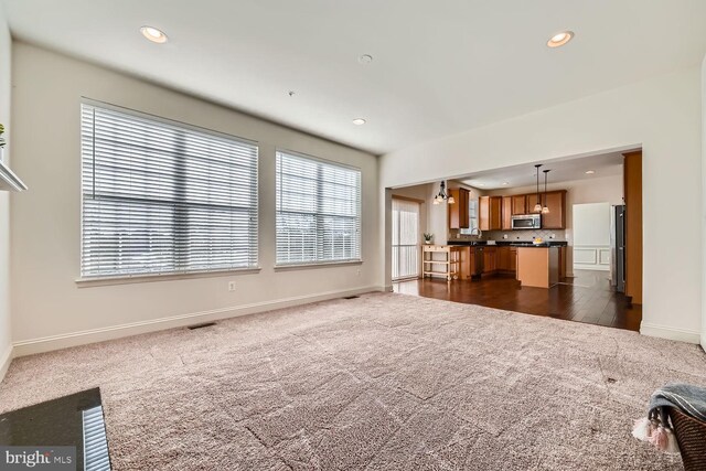 unfurnished living room featuring sink, dark carpet, and a healthy amount of sunlight