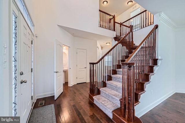 entryway with dark wood-type flooring, a high ceiling, and ornamental molding