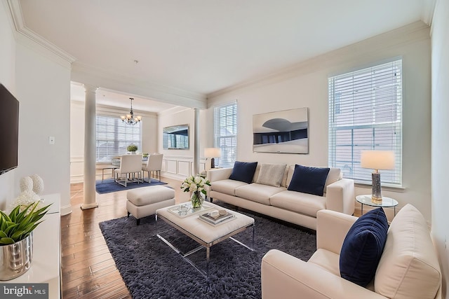 living room featuring an inviting chandelier, crown molding, hardwood / wood-style flooring, and decorative columns