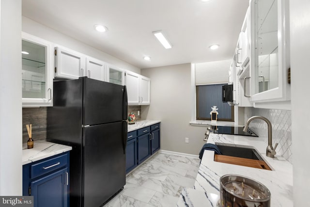 kitchen with white cabinets, black refrigerator, sink, and blue cabinetry