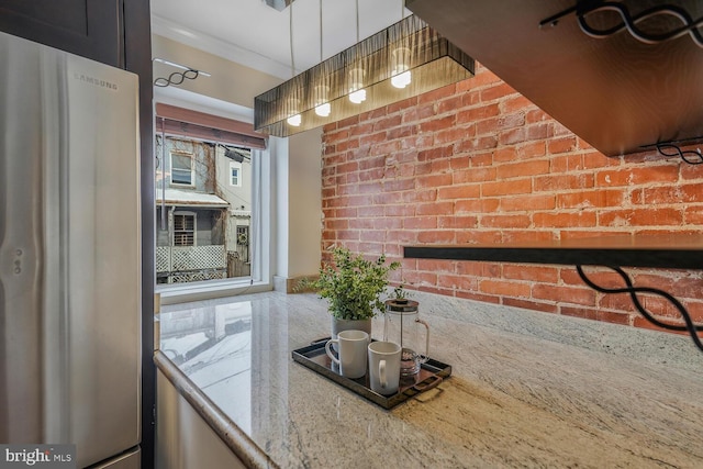 kitchen with brick wall, light stone countertops, and stainless steel refrigerator