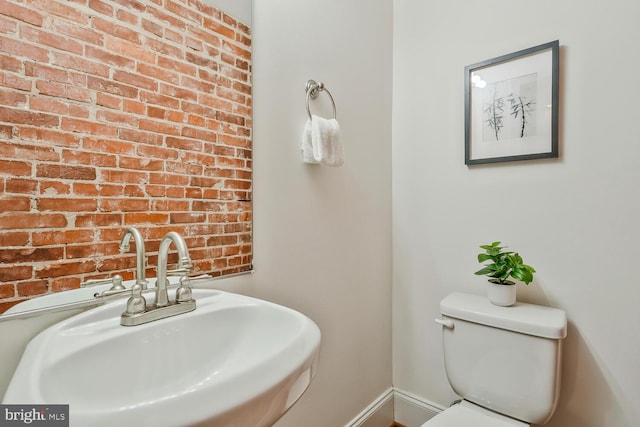 bathroom with toilet, sink, and brick wall