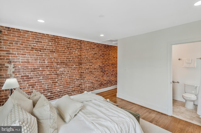 bedroom with light wood-type flooring, brick wall, and ensuite bath