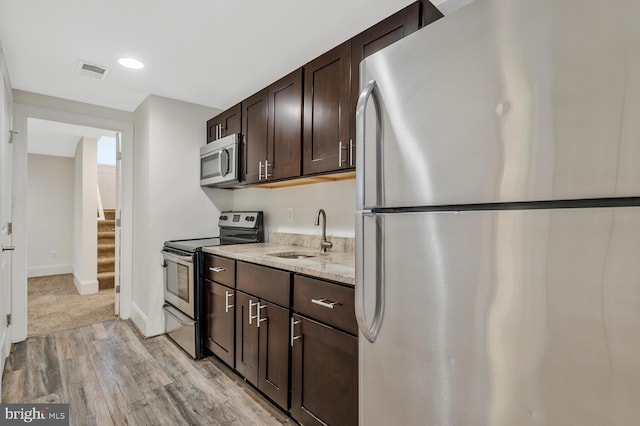 kitchen with dark brown cabinetry, light stone countertops, sink, stainless steel appliances, and light hardwood / wood-style flooring