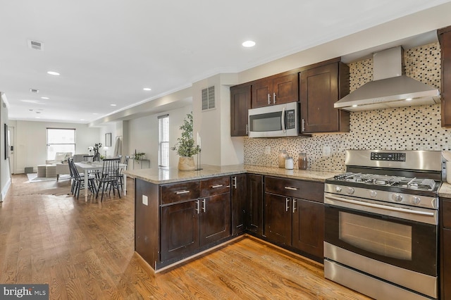 kitchen featuring kitchen peninsula, light hardwood / wood-style flooring, stainless steel appliances, and wall chimney range hood