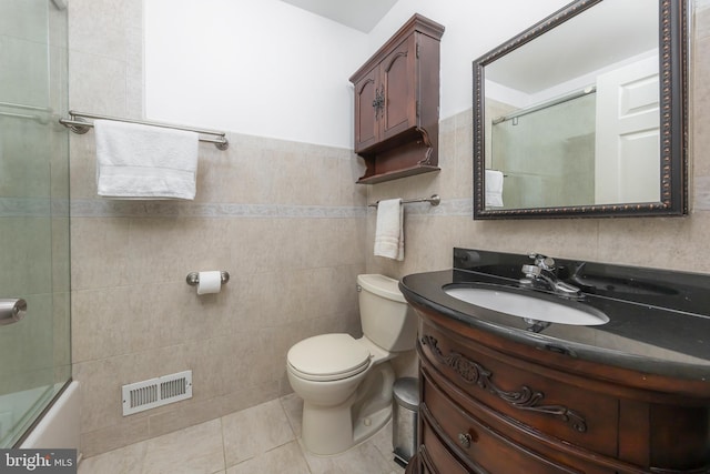 full bathroom with combined bath / shower with glass door, tile patterned floors, vanity, tile walls, and toilet