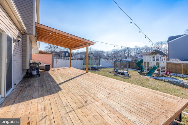 wooden terrace featuring a playground, a yard, and a trampoline