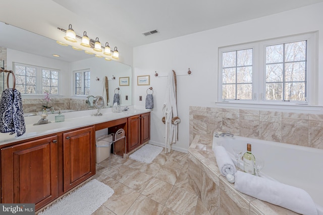 bathroom featuring vanity, a healthy amount of sunlight, and tiled tub