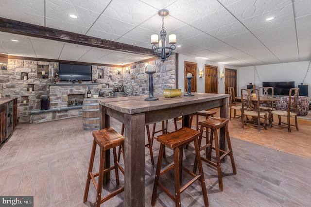 bar featuring a notable chandelier, light hardwood / wood-style floors, beamed ceiling, and a stone fireplace