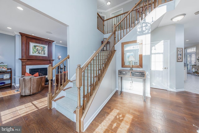 staircase with a towering ceiling, crown molding, a fireplace, and hardwood / wood-style flooring