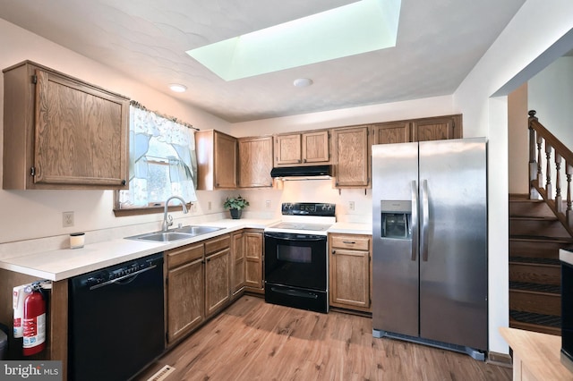 kitchen with a skylight, light hardwood / wood-style floors, sink, and black appliances