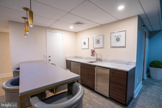 kitchen featuring fridge, sink, dark brown cabinetry, hanging light fixtures, and a paneled ceiling