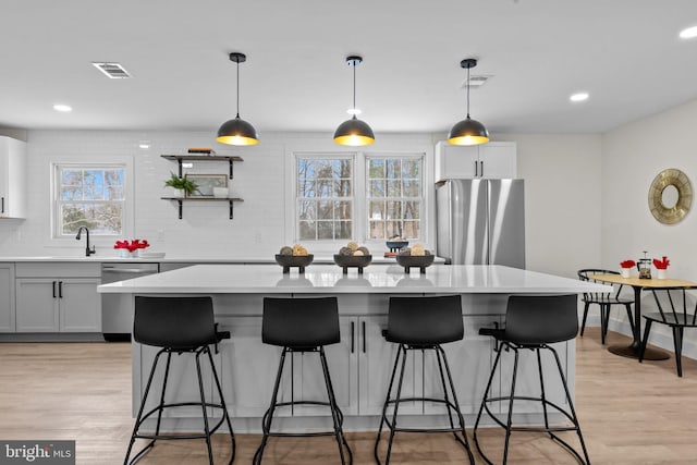 kitchen with stainless steel appliances, pendant lighting, light hardwood / wood-style flooring, white cabinets, and a center island