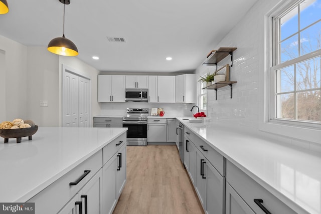 kitchen featuring backsplash, stainless steel appliances, sink, pendant lighting, and light hardwood / wood-style flooring